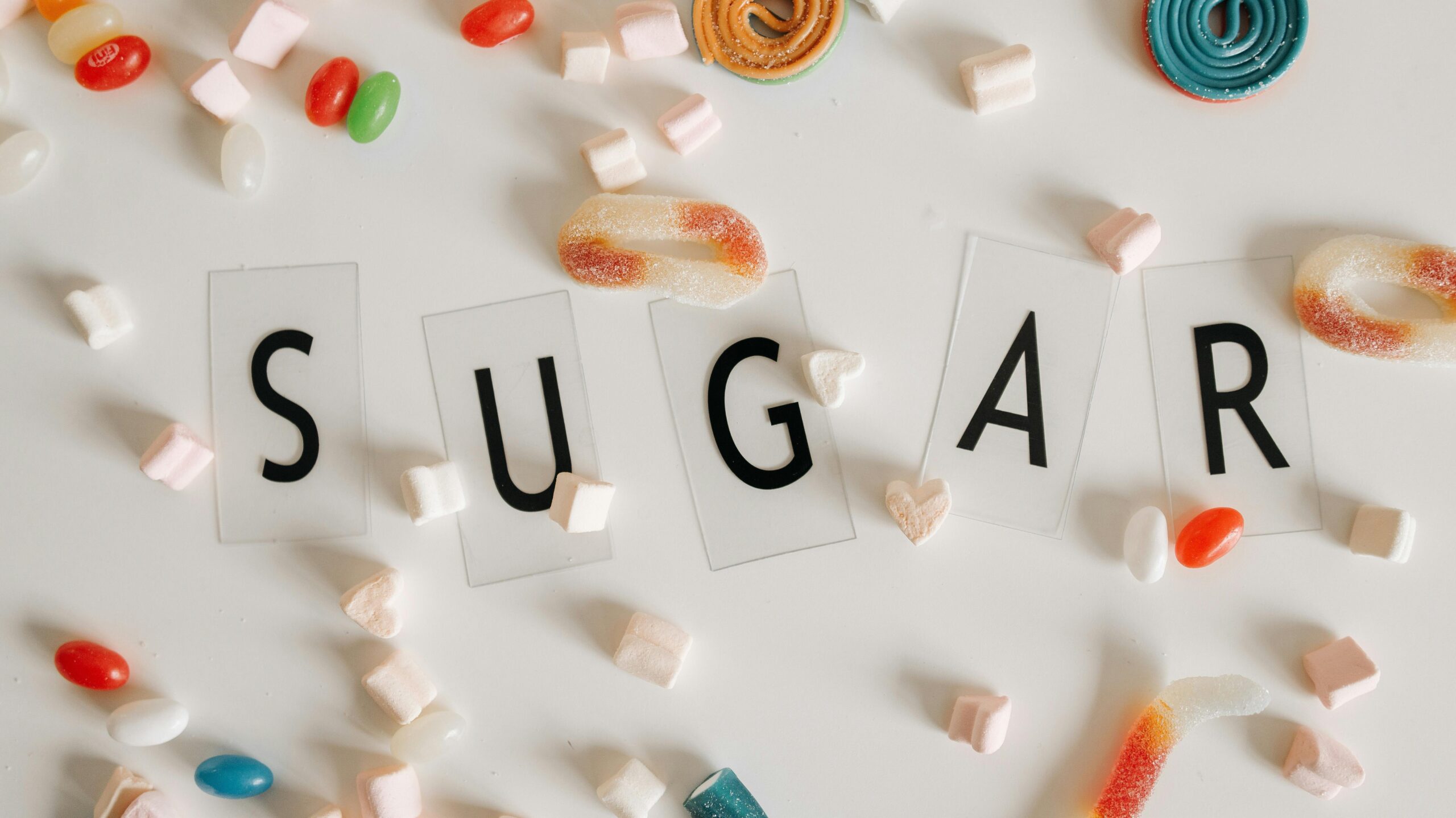 Flat lay of assorted colorful candies around the word 'SUGAR' on a white background.